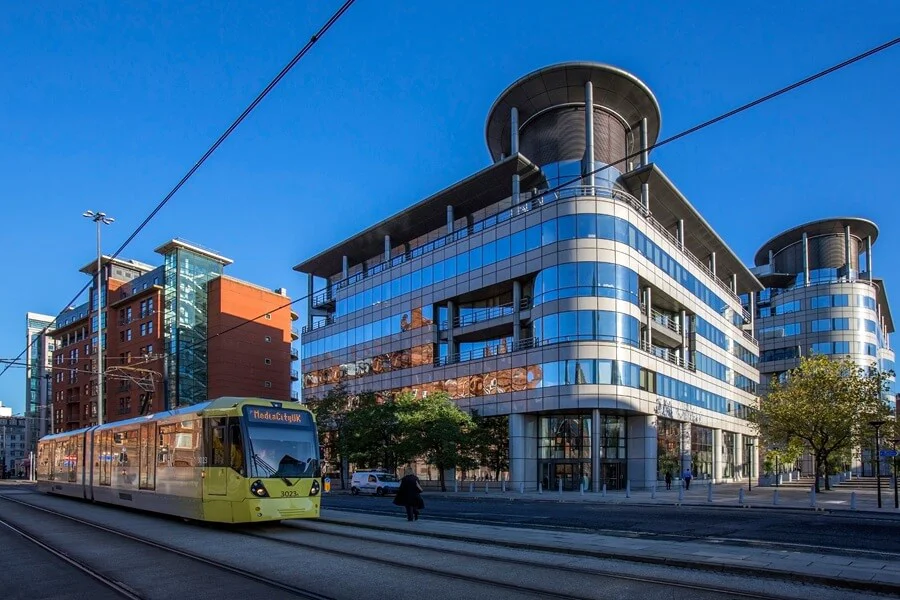 An image of a train passing a building in Manchester England.